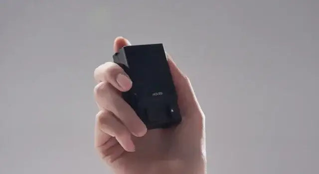 Hand håller upp svart Hover Air Beacon-enhet mot grå bakgrund