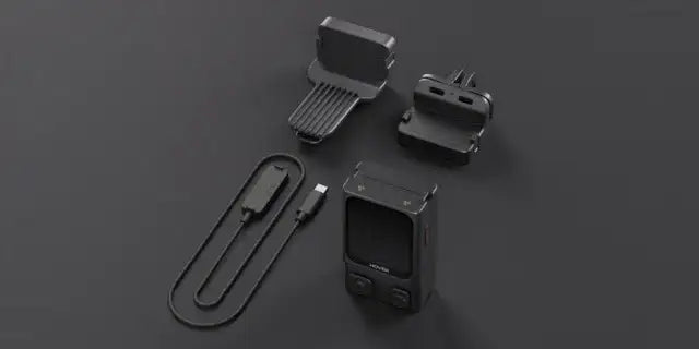 Svart bärbar enhet med två knappar och tillbehör på mörk yta, kompatibla delar och laddningskabel